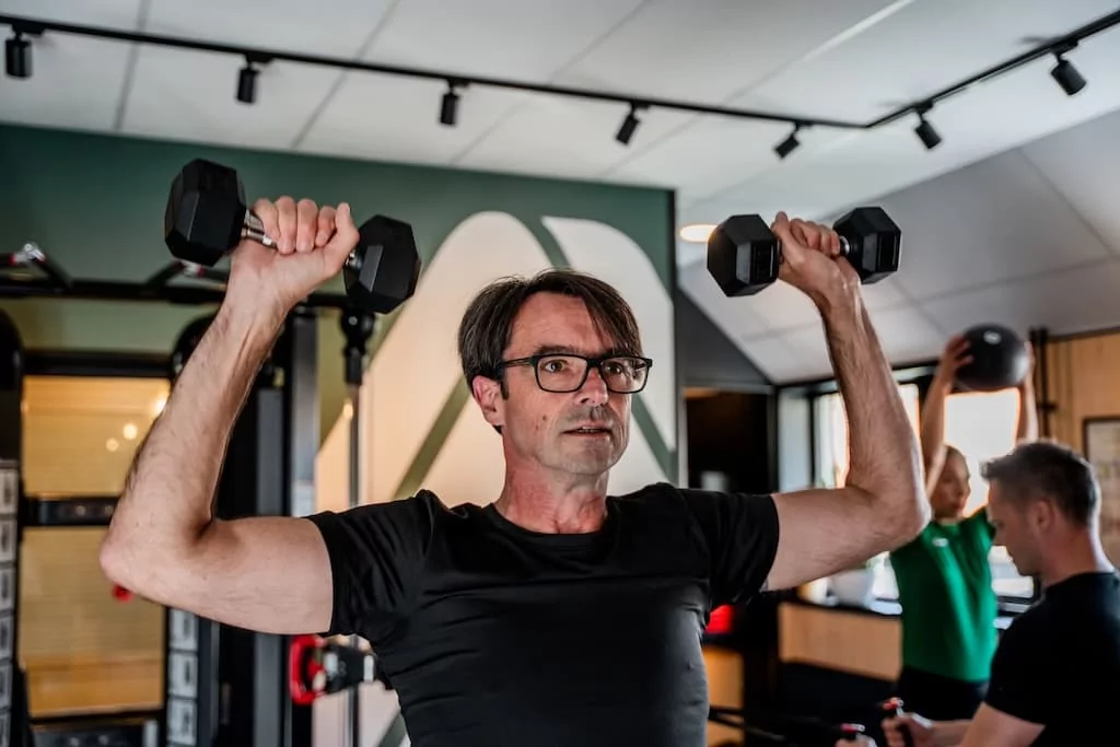 Man traint schouders met dumbbells tijdens krachttraining in de gym van Quality Lifestyle Training.