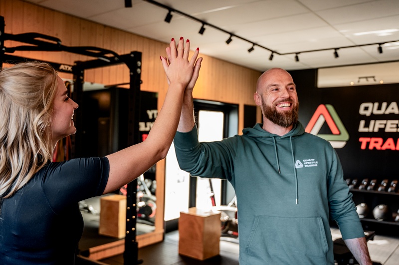 Personal trainer geeft klant een high-five na training in de gym