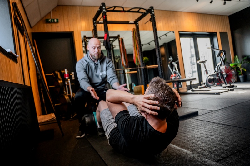 Personal trainer begeleidt klant tijdens buikspieroefening in de gym